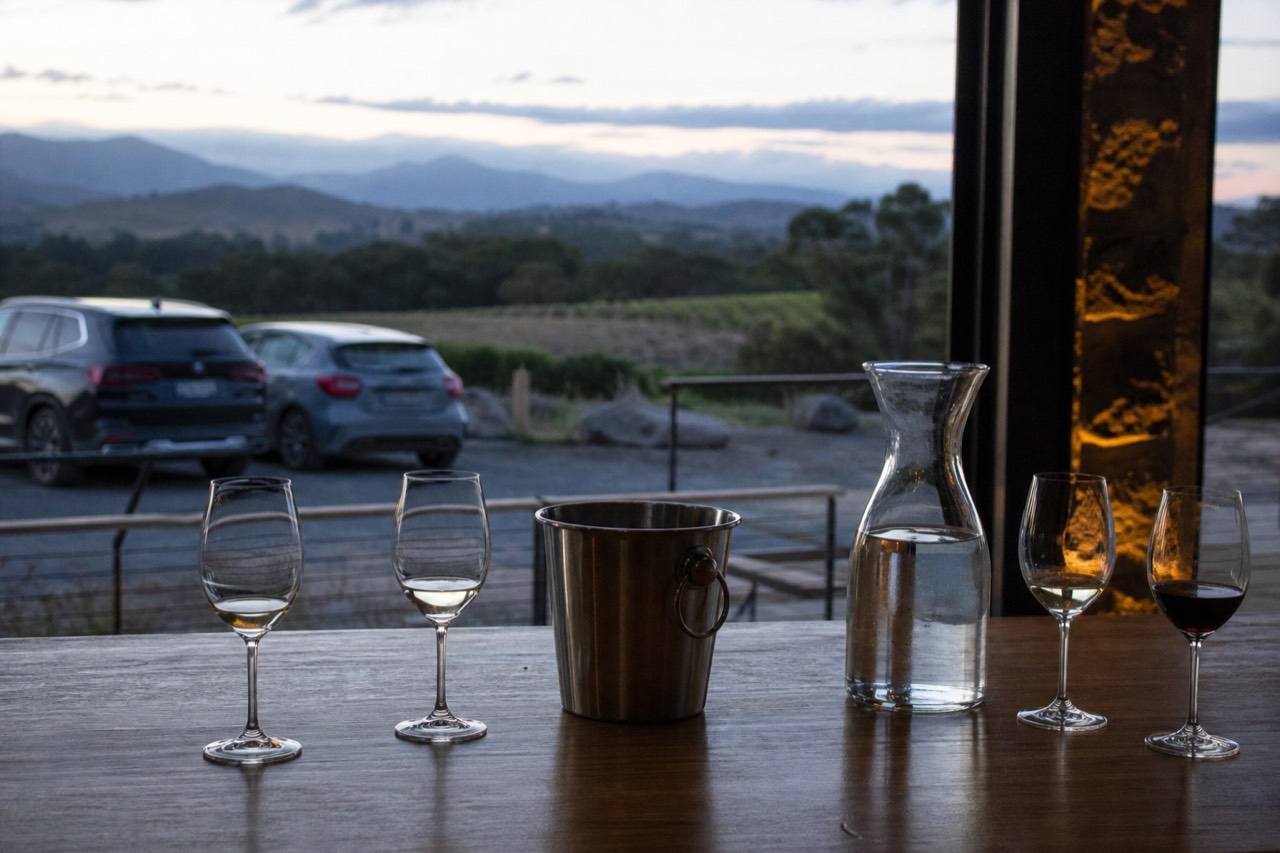 Tasting bench with a stainless spit bucket, water carafe and four glasses at different fill levels in a cellar door