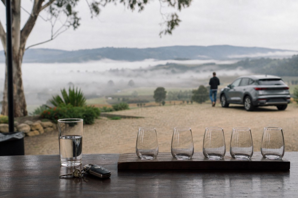 Car keys and a single glass of water beside a tasting flight on a cellar door counter, the flight untouched
