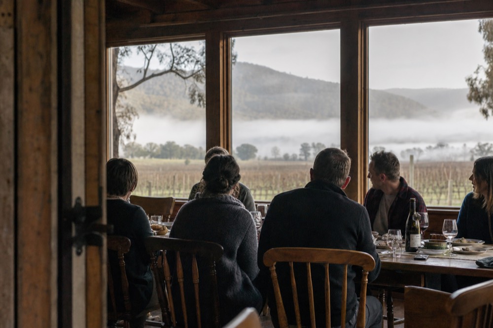 A small group of six seated at a long table in a rustic country store dining room with wine glasses and shared plates